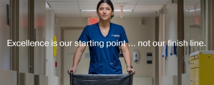 woman in blue scrubs pushes empty wheelchair in hospital corridor; text overlay: Excellence is our starting point ... not our finish line.