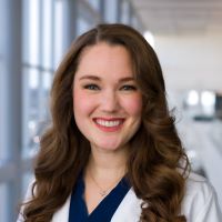 woman smiling with black hair, wearing medical coat