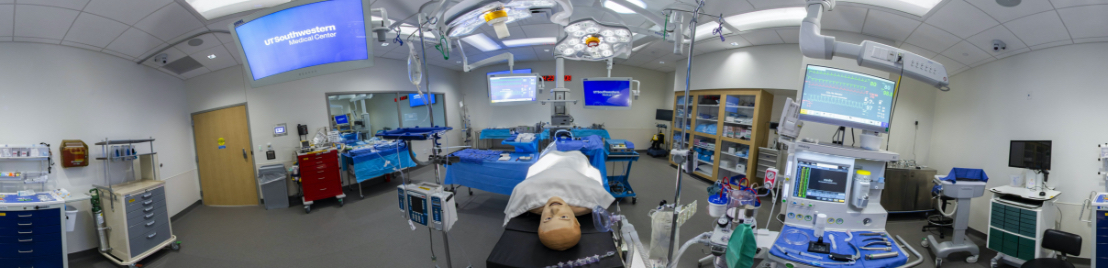 A simulation room with a model on a bed in the center and medical equipment around the room