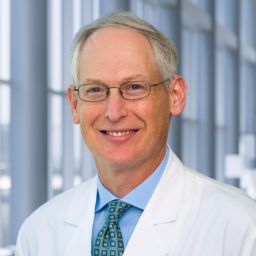 Dr. Mark Drazner wearing a light blue shirt witha a patterned tie and a white lab coat standing in the Clements University Hospital lobby