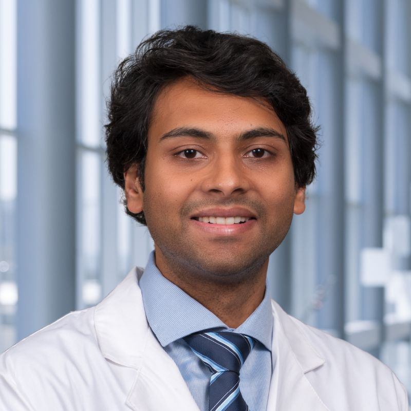 Dr. Vinayak Subramanian wearing glasses, a blue shirt with a striped tie and a white lab coat standing in the Clements University Hospital lobby