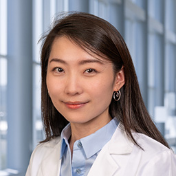 Dr. Simeng Wang wearing a light blue shirt, and a white lab coat standing in the Clements University Hospital lobby
