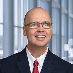 Dr. George Jackwon wearing glasses and a dark suit standing in the Clements University Hospital lobby