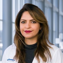 Dr. Aimaz Afrough wearing a black shirt and a white lab coat standing in the Clements University Hospital lobby