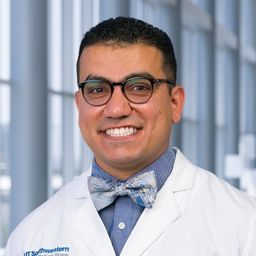 Dr. Salwan Al Mutar wearing a blue shirt with a blue bow tie and a white lab coat standing in the Clements University Hospital lobby