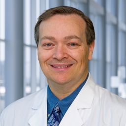 Dr. Larry Anderson wearing a blue shirt with a blue pattrened tie and a white lab coat standing in the Clements University Hospital lobby