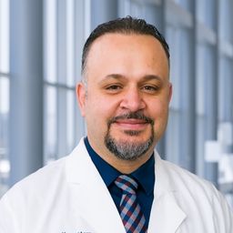 Dr. Waddah Arafat wearing a dark blue shirt with a blue stiped tie and a white lab coat standing in the Clements University Hospital lobby