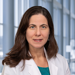 Dr. Arin Aurora wearing a green shirt and a white lab coat standing in the Clements University Hospital lobby