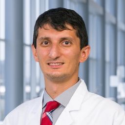 Dr. Taha Bat wearing a grey shirt with a red tie and a white lab coat standing in the Clements University Hospital lobby