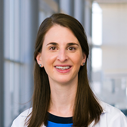 Dr. Natalie Bavli wearing a blue shirt and a white lab coat standing in the Clements University Hospital lobby