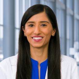 Dr. Sheena Bhalla wearing a bright blue shirt and a white lab coat standing in the Clements University Hospital lobby