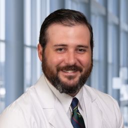 Dr. Timothy Brown wearing a white shirt with a dark tie and a white lab coat standing in the Clements University Hospital lobby