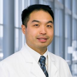 Dr. Issac Chan wearing a white shirt with a blue stiped tie and a white lab coat standing in the Clements University Hospital lobby