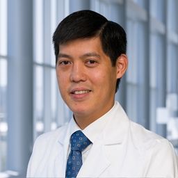 Dr. Stephen Chung wearing a white shirt with a blue patterned tie and a white lab coat standing in the Clements University Hospital lobby