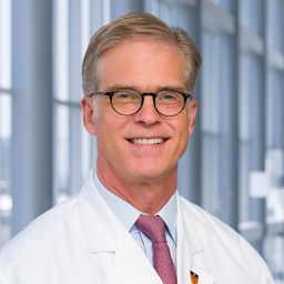 Dr. Robert Collins wearing a light blue shirt with a patterend tie and a white lab coat standing in the Clements University Hospital lobby