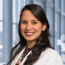 Dr. Glenda Delgado Ramos wearing a patterned shirt and a white lab coat standing in the Clements University Hospital lobby