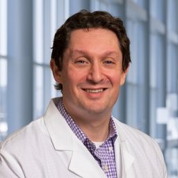 Dr. Ben Drapkin wearing a purple checkered shirt and a white lab coat standing in the Clements University Hospital lobby