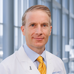 Dr. David Gerber wearing a light blue shirt with a yellow tie and a white lab coat standing in the Clements University Hospital lobby