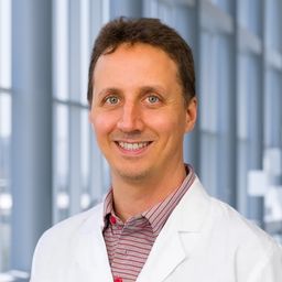 Dr. Joshua Gruber wearing a stiped shirt and a white lab coat standing in the Clements University Hospital lobby