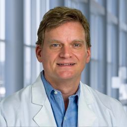 Dr. Hans Hammers wearing a blue shirt and a white lab coat standing in the Clements University Hospital lobby