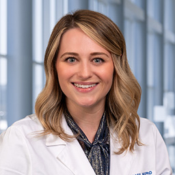 Dr. Lindsay Hill wearing a patterned shirt, and a white lab coat standing in the Clements University Hospital lobby