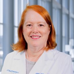 Dr. Sandra Hofmann wearing a grey shirt and a white lab coat standing in the Clements University Hospital lobby