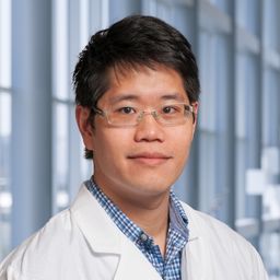 Dr. David Hsieh wearing a blue checkered shirt and a white lab coat standing in the Clements University Hospital lobby