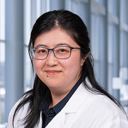 Dr. Eileen Hu wearing glasses, a dark blue shirt, and a white lab coat standing in the Clements University Hospital lobby