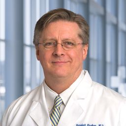 Dr. Randall Hughes wearing a white shirt with a green striped tie and a white lab coat standing in the Clements University Hospital lobby