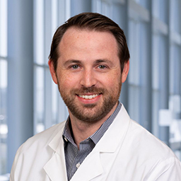 Dr. Jackson Clayton wearing a frey shirt and a white lab coat standing in the Clements University Hospital lobby