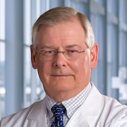 Dr. David H. Johnson wearing a checkered shirt with a patterned tie and a white lab coat standing in the Clements University Hospital lobby
