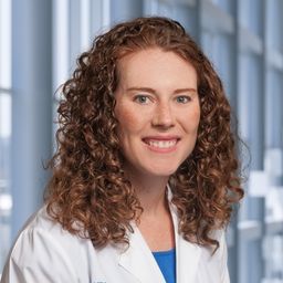 Dr. Amy Jones wearing a turquoise shirt and a white lab coat standing in the Clements University Hospital lobby