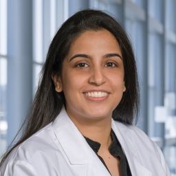 Dr. Radhika Kainthla wearing a black shirt and a white lab coat standing in the Clements University Hospital lobby