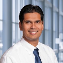 Dr. Syed Kazmi wearing a white shirt and dark blue tie standing in the Clements University Hospital lobby