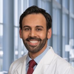 Dr. Adeel Khan wearing a light blue shirt with a dark red tie and a white lab coat standing in the Clements University Hospital lobby