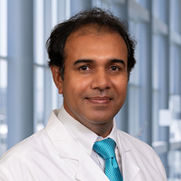 Dr. Arvind Kumar wearing a white shirt with bright blue tie and a white lab coat standing in the Clements University Hospital lobby