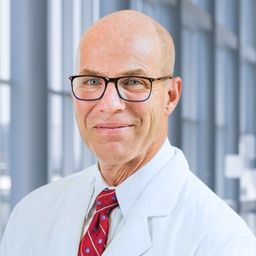 Dr. Jay Lohrey wearing a white shirt with a red stiped tie and a white lab coat standing in the Clements University Hospital lobby