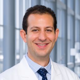 Dr. Yazan Madanat wearing a light blue shirt with a dark tie and a white lab coat standing in the Clements University Hospital lobby