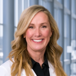 Dr. Heather McArthur wearing a black shirt and a white lab coat standing in the Clements University Hospital lobby