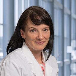 Dr. Amanda Mennie wearing a patterned shirt, and a white lab coat standing in the Clements University Hospital lobby