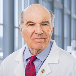 Dr. John Minna wearing a blue shirt with a red tie and a white lab coat standing in the Clements University Hospital lobby