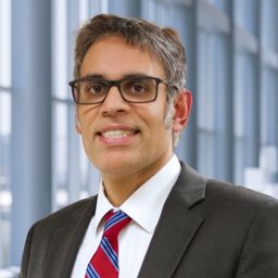 Dr. Deepak Nijhawan wearing a white shirt, a red and blue stiped tie and dark suit jacket standing in the Clements University Hospital lobby