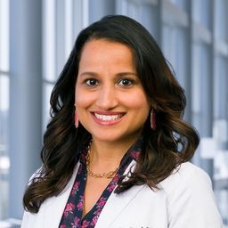 Dr. Ina Patel wearing a dark floral shirt and a white lab coat standing in the Clements University Hospital lobby