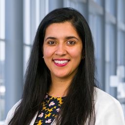 Dr. Namrata Peswani wearing a floral patterned shirt and a white lab coat standing in the Clements University Hospital lobby
