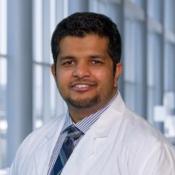 Dr. Praveen Ramakrishnan Geethakumari wearing a striped shirt with a plaid tie and a white lab coat standing in the Clements University Hospital lobby