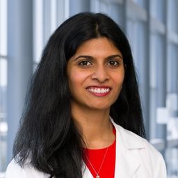 Dr. Sangeetha Reddy wearing a red shirt and a white lab coat standing in the Clements University Hospital lobby