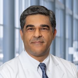 Dr. Navid Sadeghi wearing a white shirt withe a blue patterned tie and a white lab coat standing in the Clements University Hospital lobby