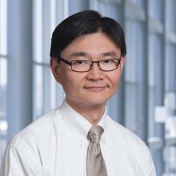 Dr. Yu-Min Shen wearing a white shirt with a grey tie and a white lab coat standing in the Clements University Hospital lobby