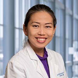 Dr. Christine Shiang wearing a pruple shirt and a white lab coat standing in the Clements University Hospital lobby