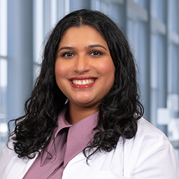 Dr. Arthi Sridhar wearing a rose colored shirt and a white lab coat standing in the Clements University Hospital lobby